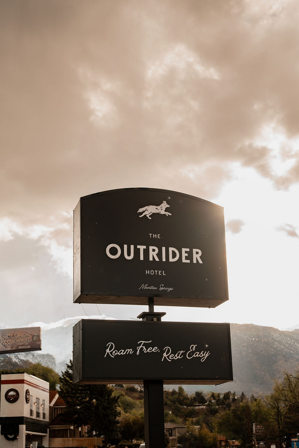 The Outrider Hotel roadside sign reading Roam Free, Rest Easy against a dramatic stormy sky in Manitou Springs