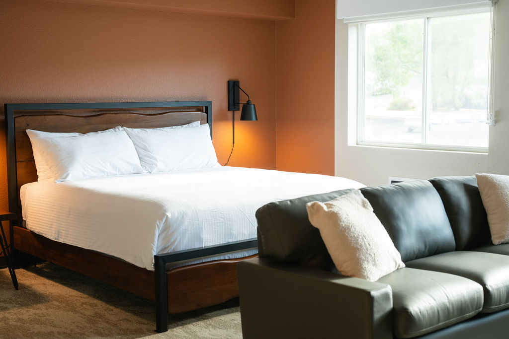 King bedroom at The Outrider Hotel with terracotta accent wall, wood headboard, and leather sofa