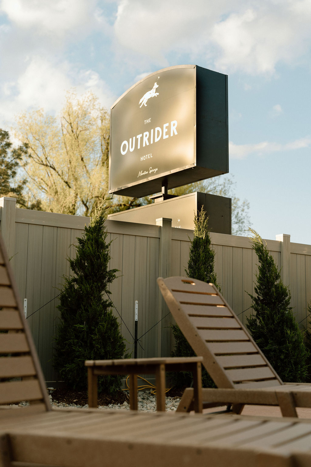 The Outrider Hotel illuminated sign with Adirondack chairs in the foreground and blue sky