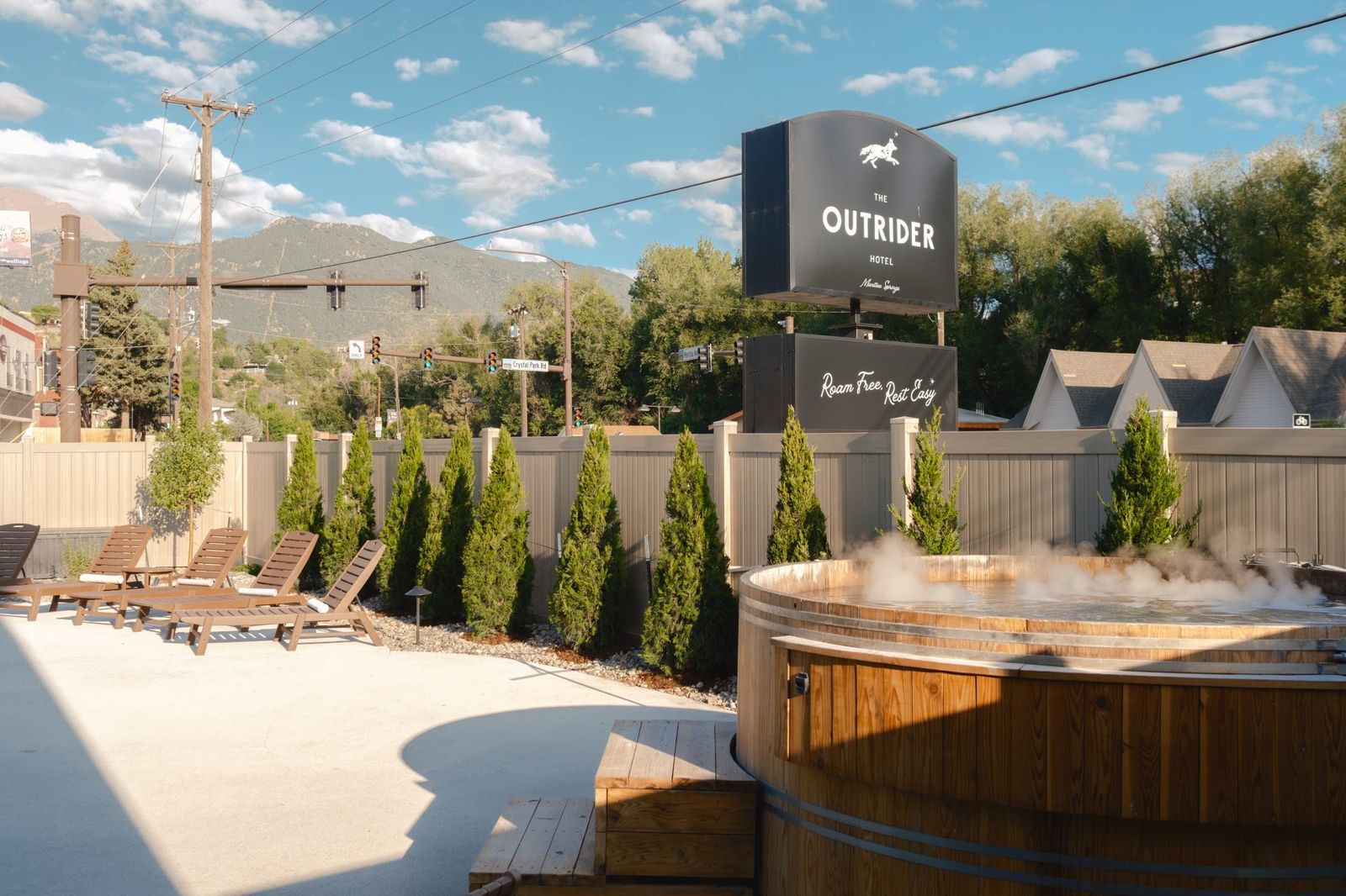 Steaming cedar hot tub on the pool deck below The Outrider Hotel sign, with mountain views