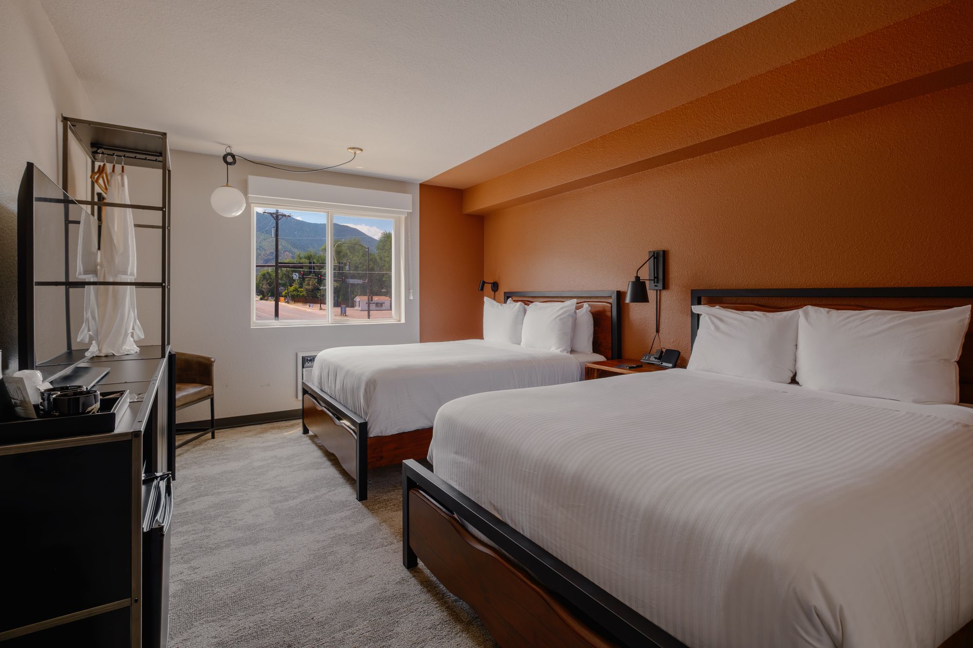 Classic Double Queen room at The Outrider Hotel with two queen beds, terracotta accent wall, and a mountain-view window