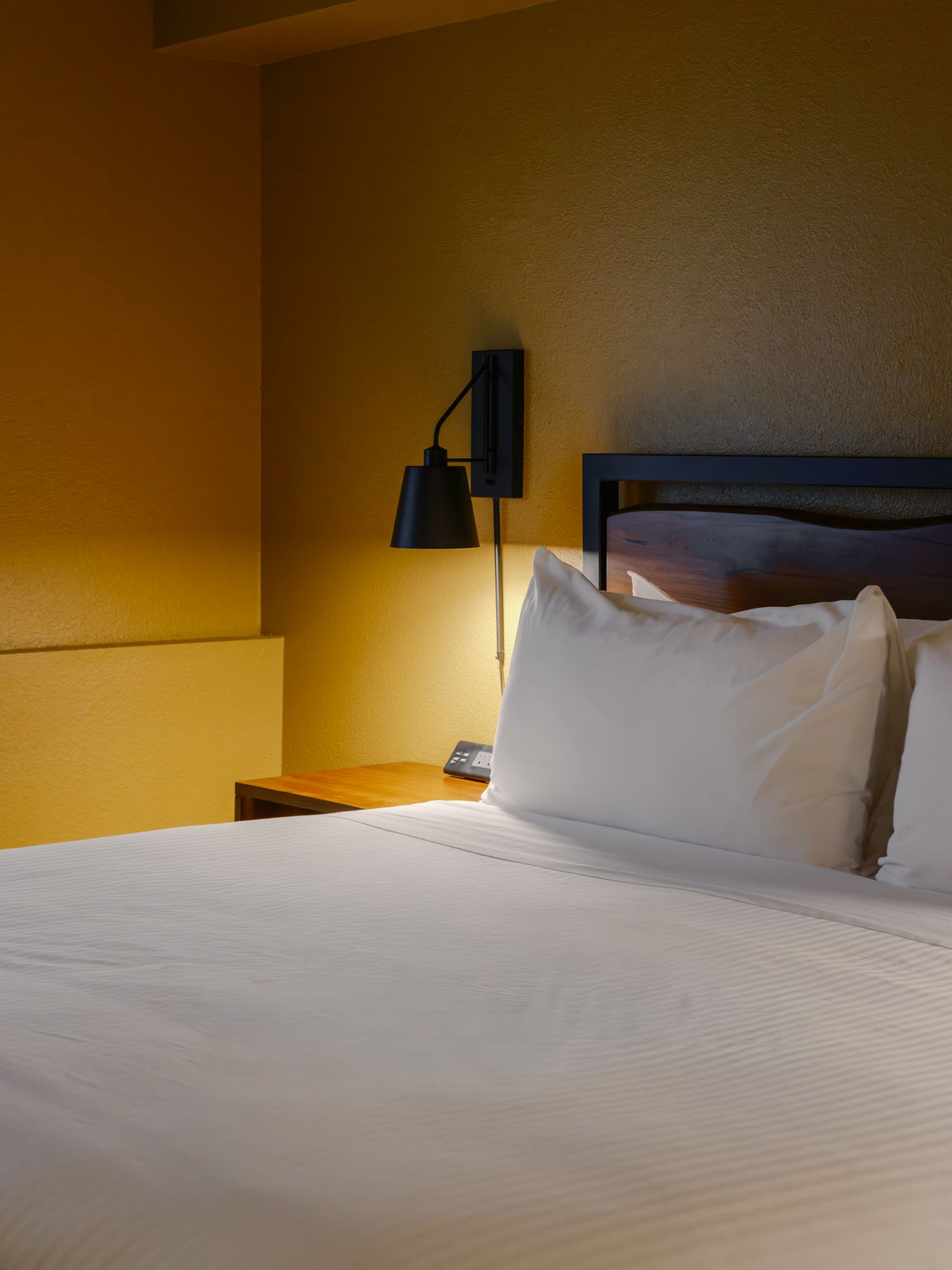 Black bedside sconce above a king bed with white linens in a Classic King room at The Outrider Hotel, Manitou Springs