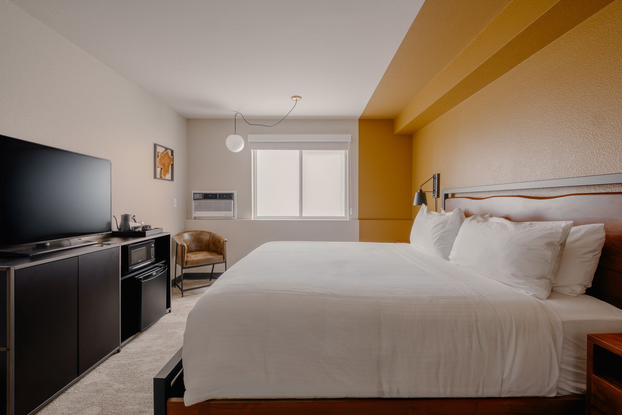 King bed facing a smart TV console with mini-fridge and coffee station in a Classic King room at The Outrider Hotel