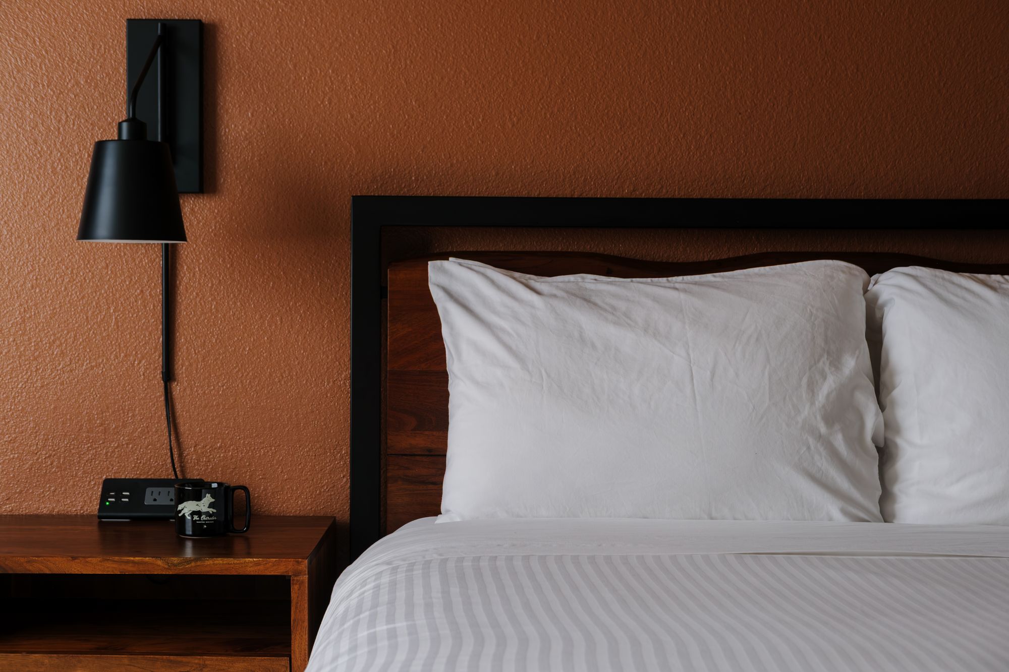 Bedside reading lamp, walnut nightstand, and crisp white queen bedding in a Classic Queen room at The Outrider Hotel
