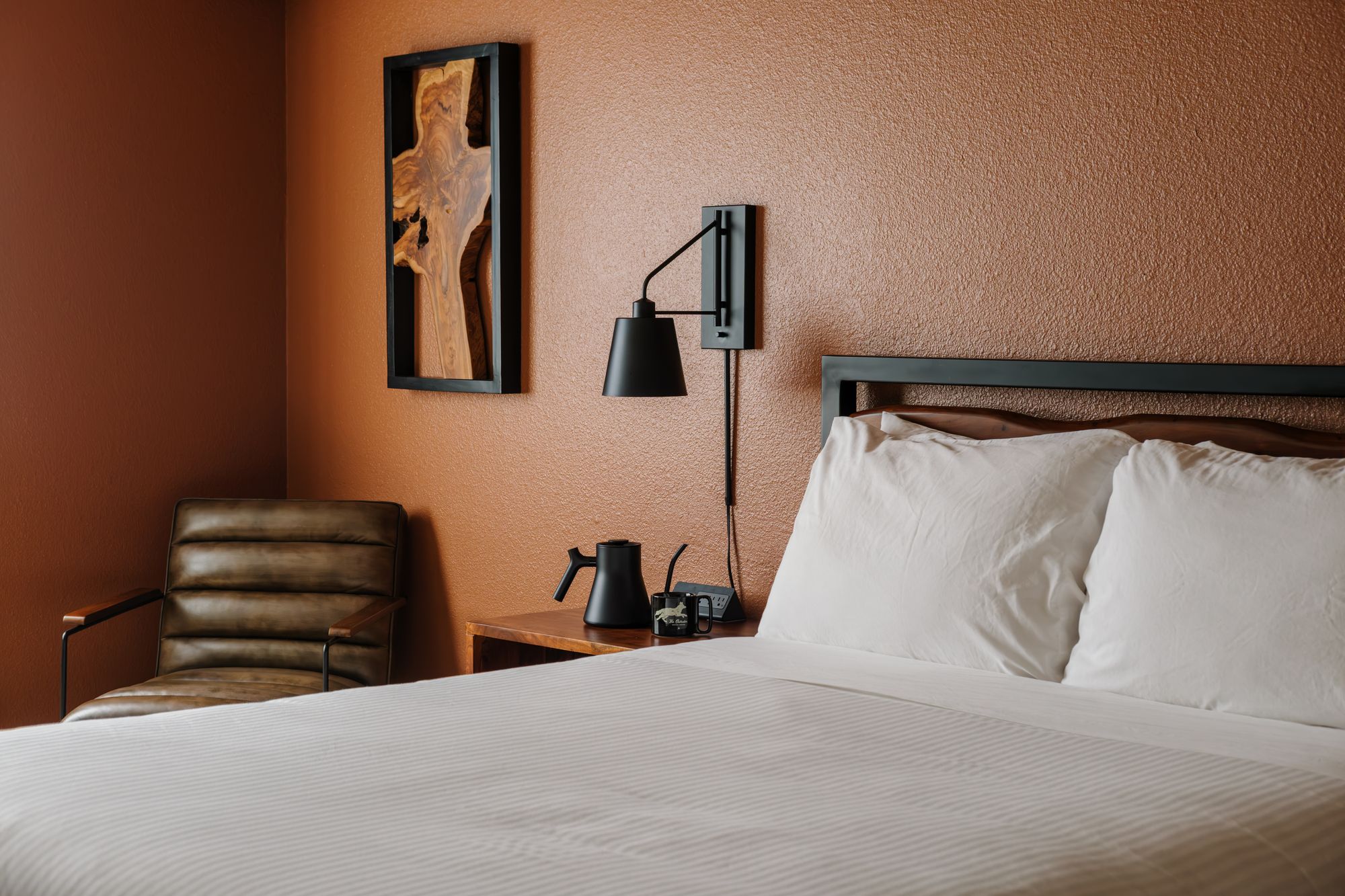 Queen bed, leather reading chair, and pour-over kettle against a terracotta wall in a Classic Queen room at The Outrider Hotel