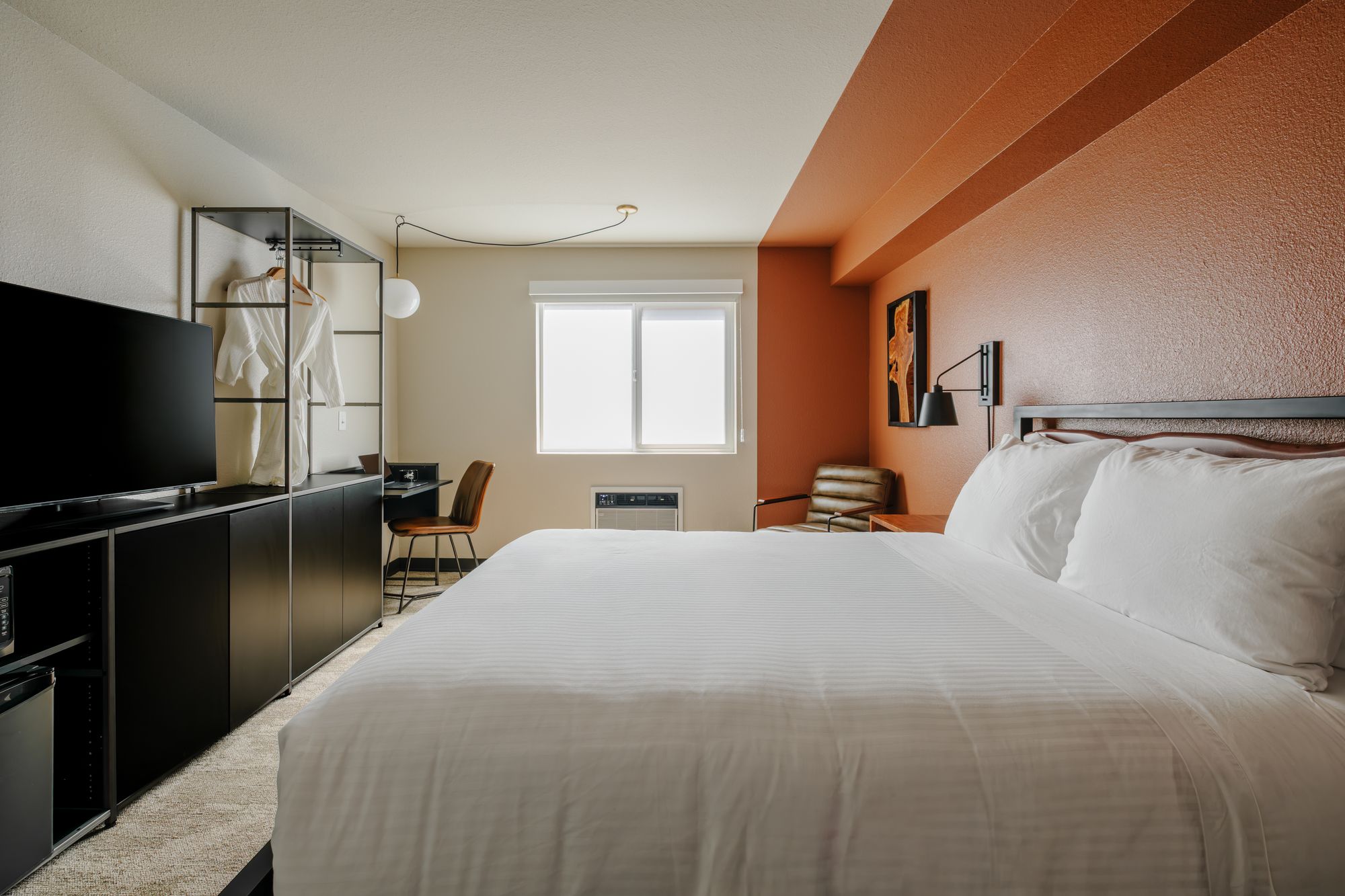 Classic Queen room with open steel wardrobe, robe, smart TV console, and queen bed at The Outrider Hotel, Manitou Springs