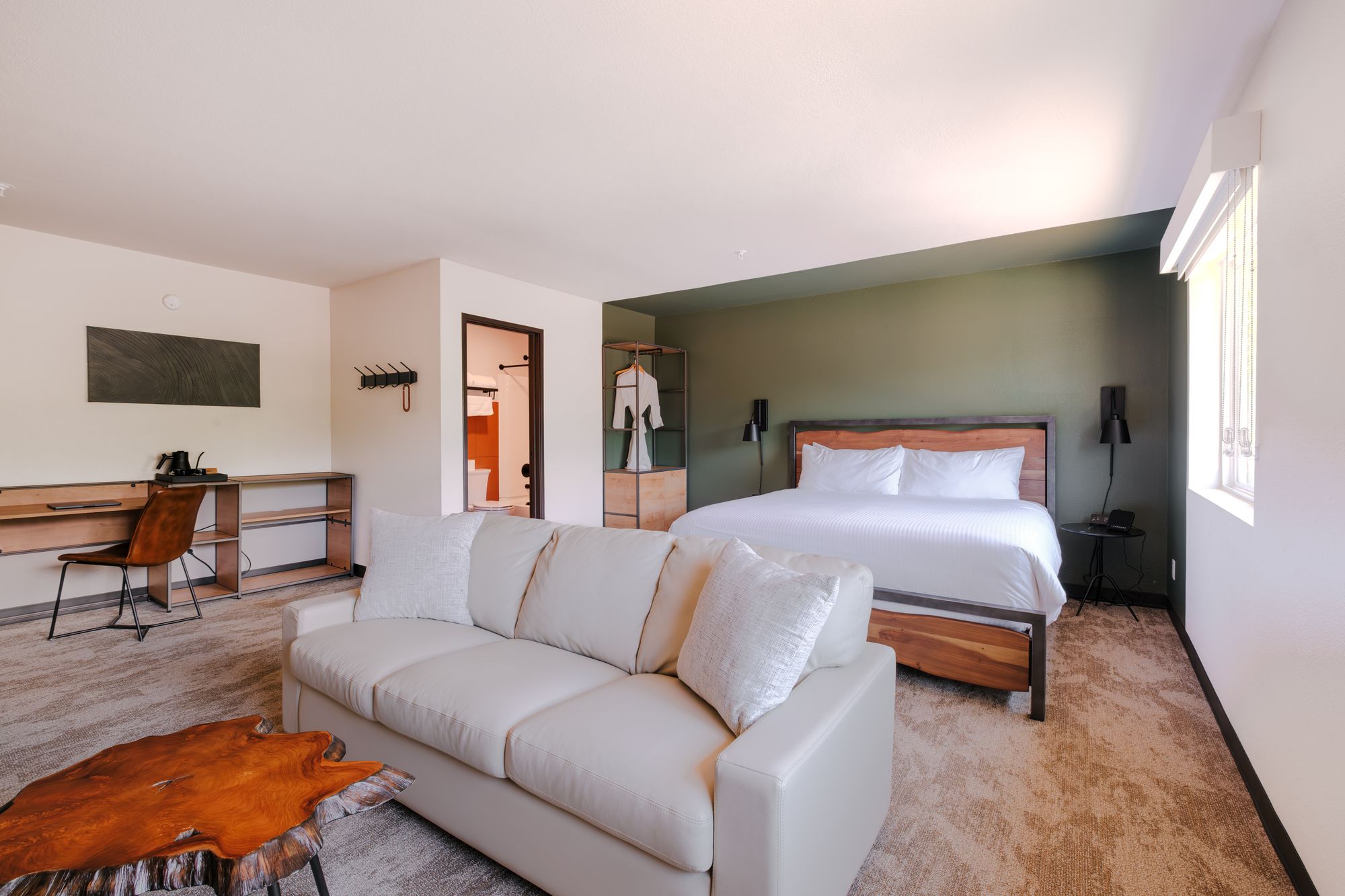 Grand King Suite seating area with cream sofa, live-edge coffee table, writing desk, and king bed at The Outrider Hotel