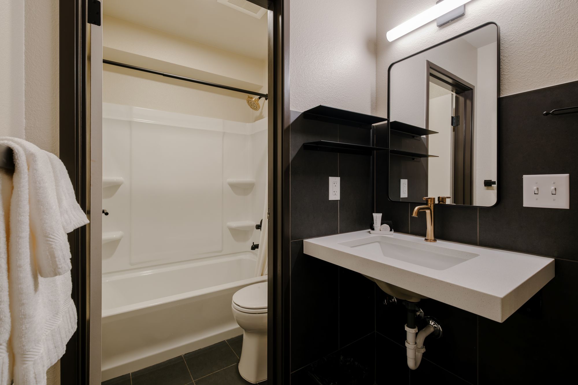 Guest bathroom with black tile, floating vanity, and walk-in tub-shower at The Outrider Hotel, Manitou Springs