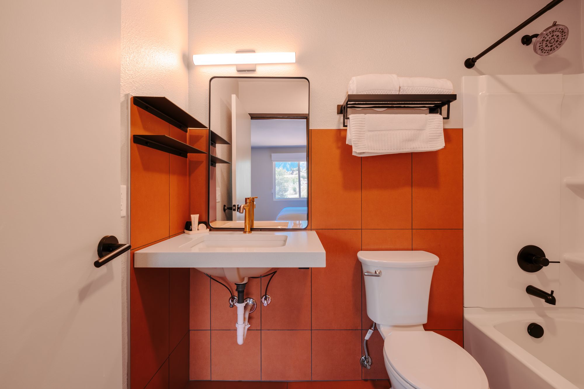 Guest bathroom with copper-tone tile, floating vanity, brass faucet, and tub-shower at The Outrider Hotel