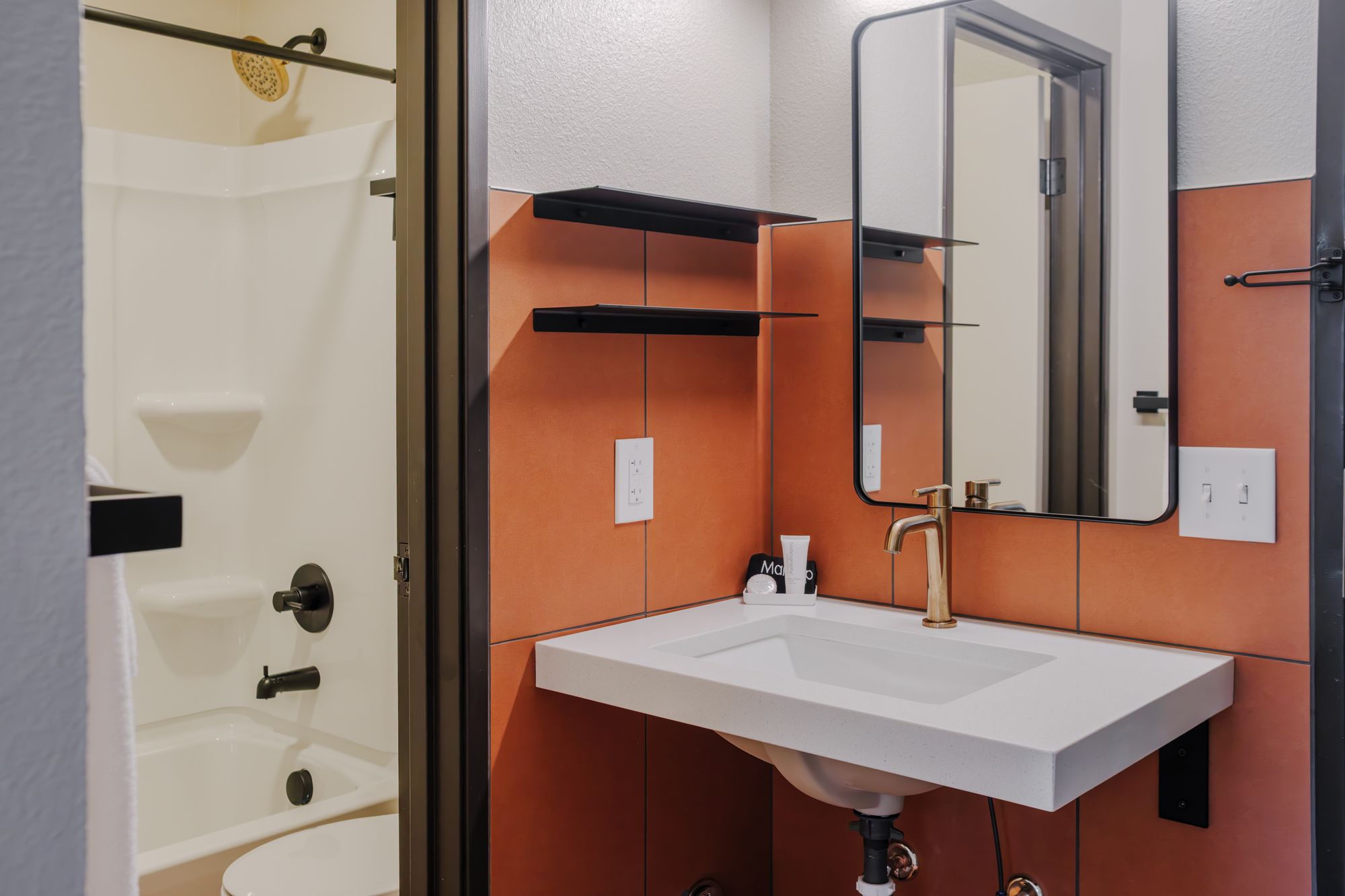 Floating white vanity with brushed brass faucet and copper tile backsplash in an Outrider Hotel guest bathroom