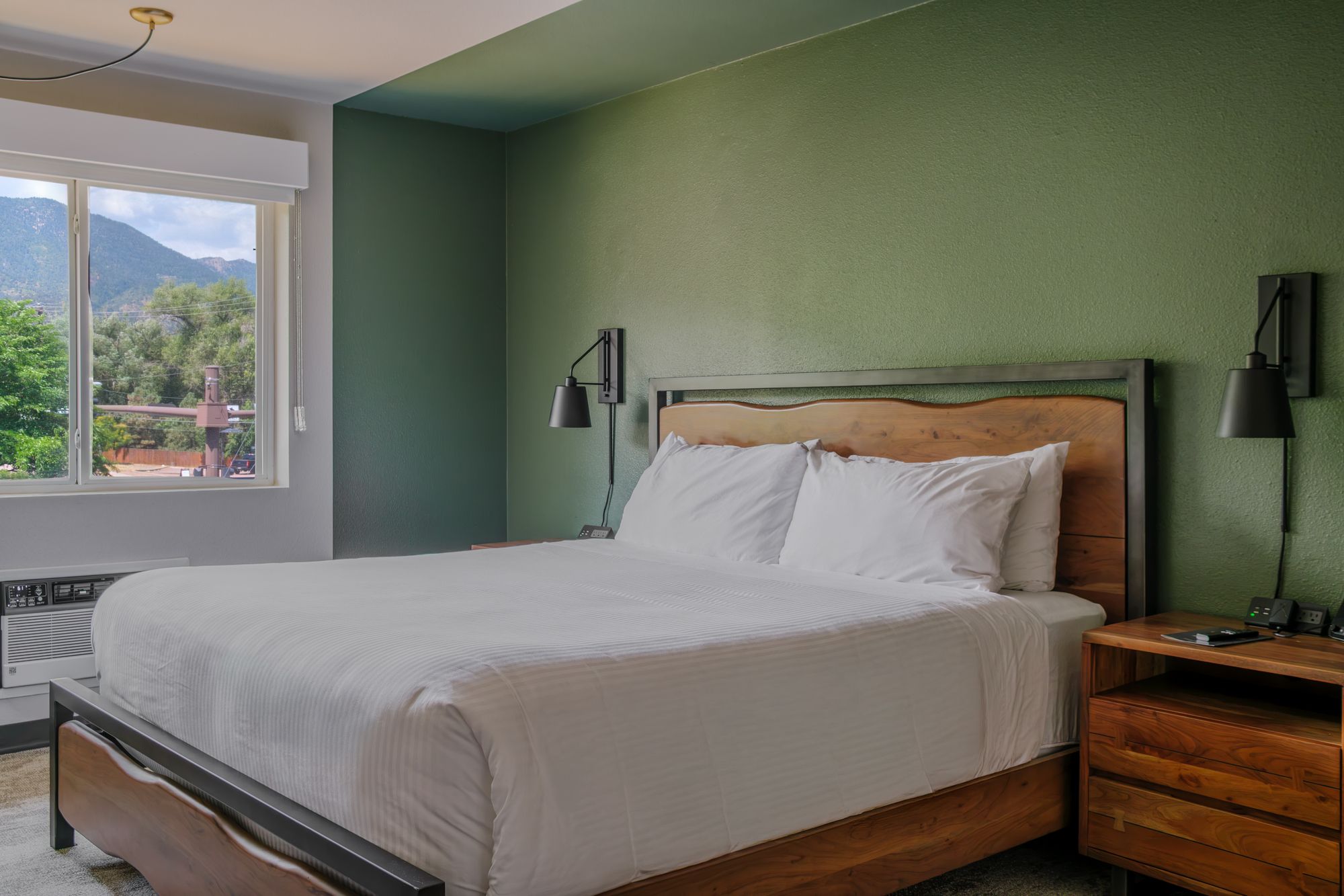 King guest room with sage green accent wall and a window view of the Front Range at The Outrider Hotel in Manitou Springs