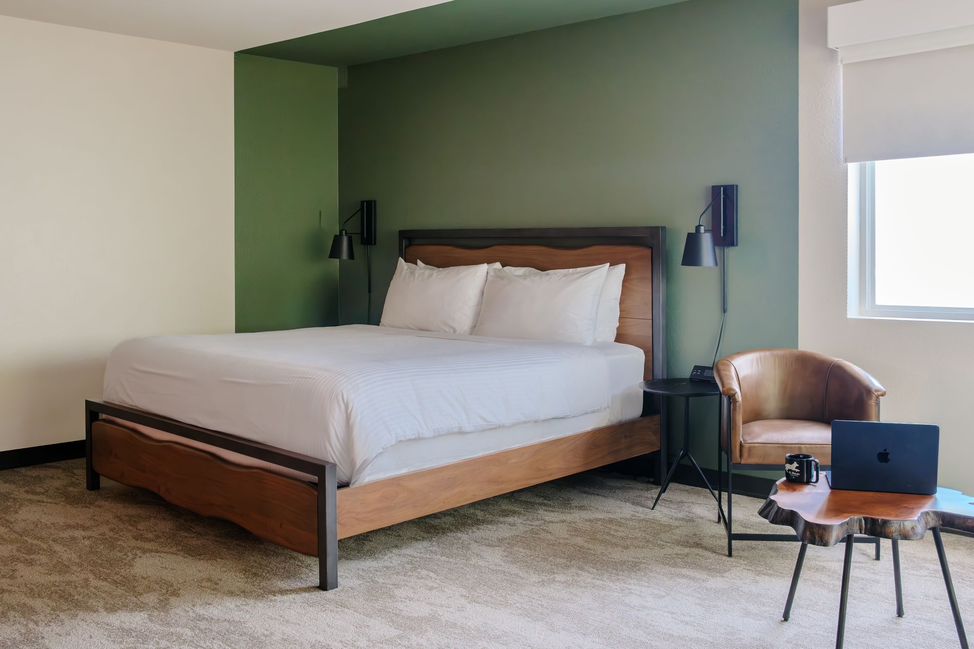 King guest room with sage green accent wall, leather club chair, and live-edge side table at The Outrider Hotel
