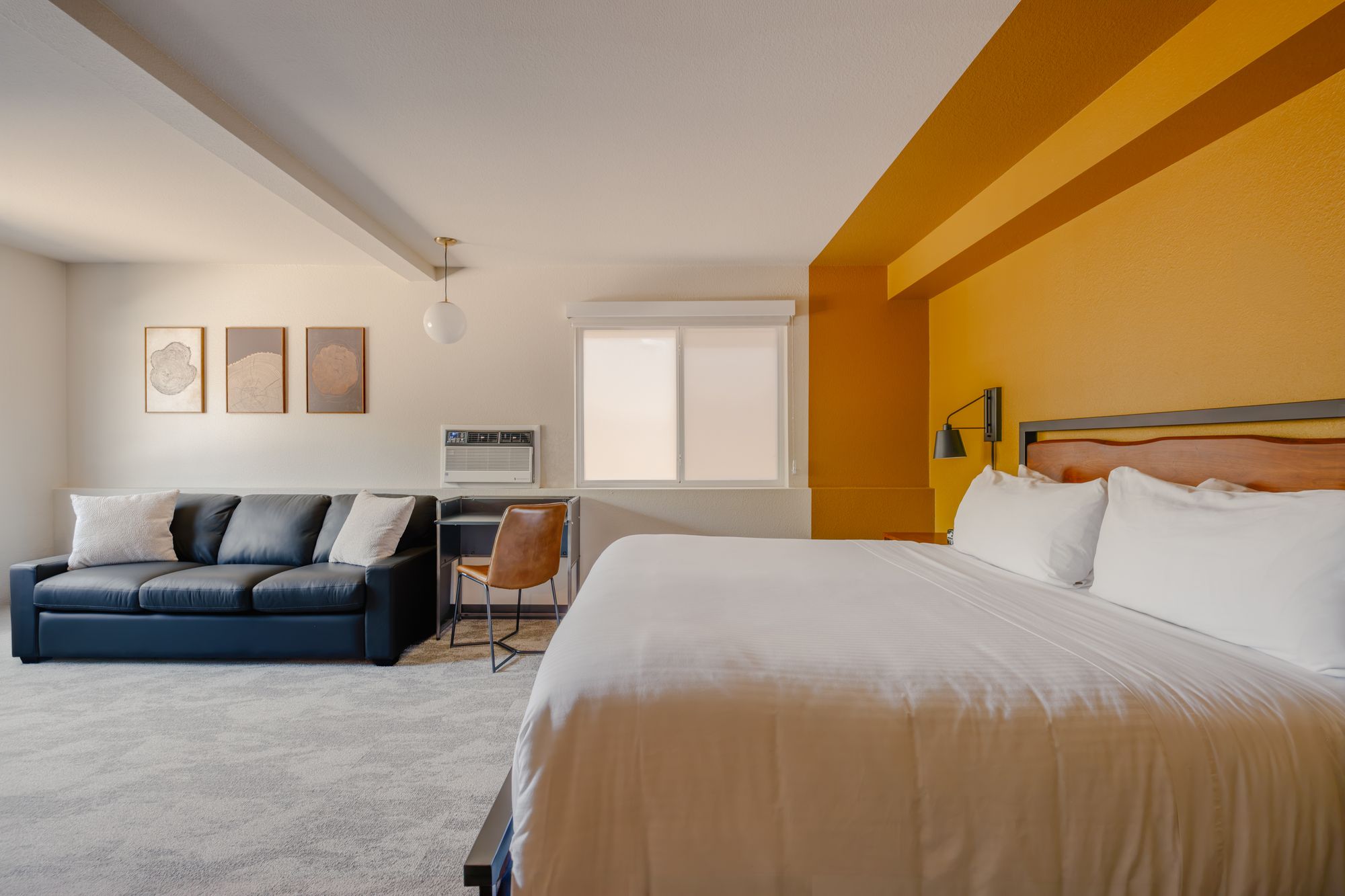 King guest room with mustard accent wall, navy leather sofa, and writing desk at The Outrider Hotel, Manitou Springs