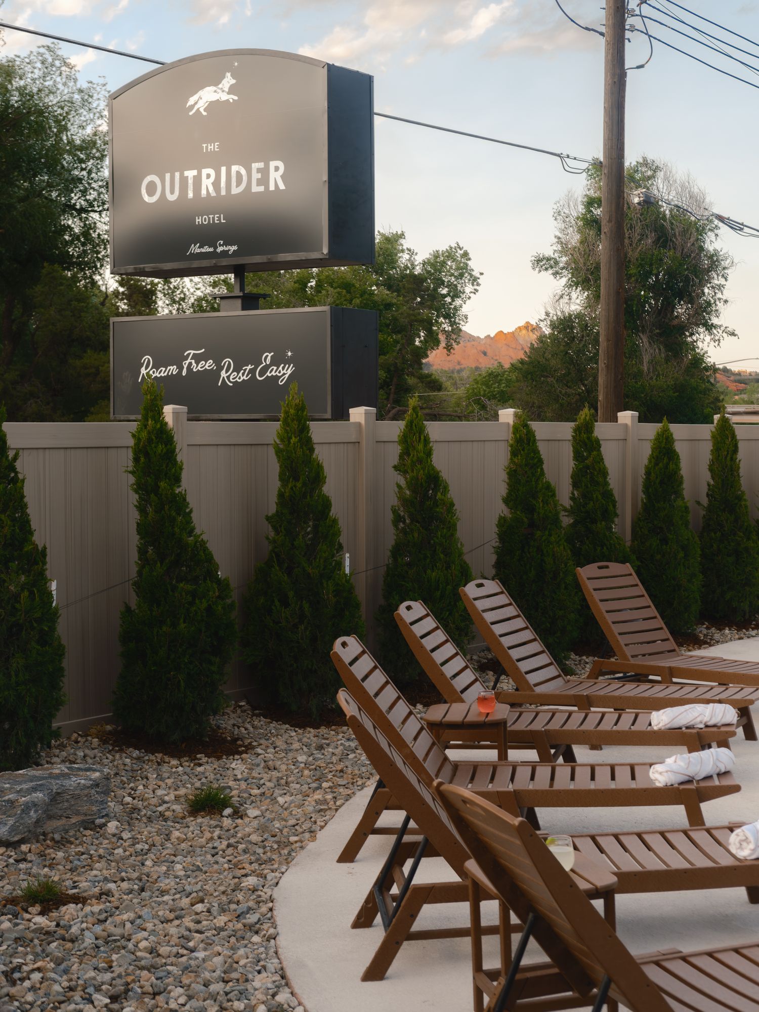 Row of wooden lounge chairs on the pool deck below The Outrider Hotel sign